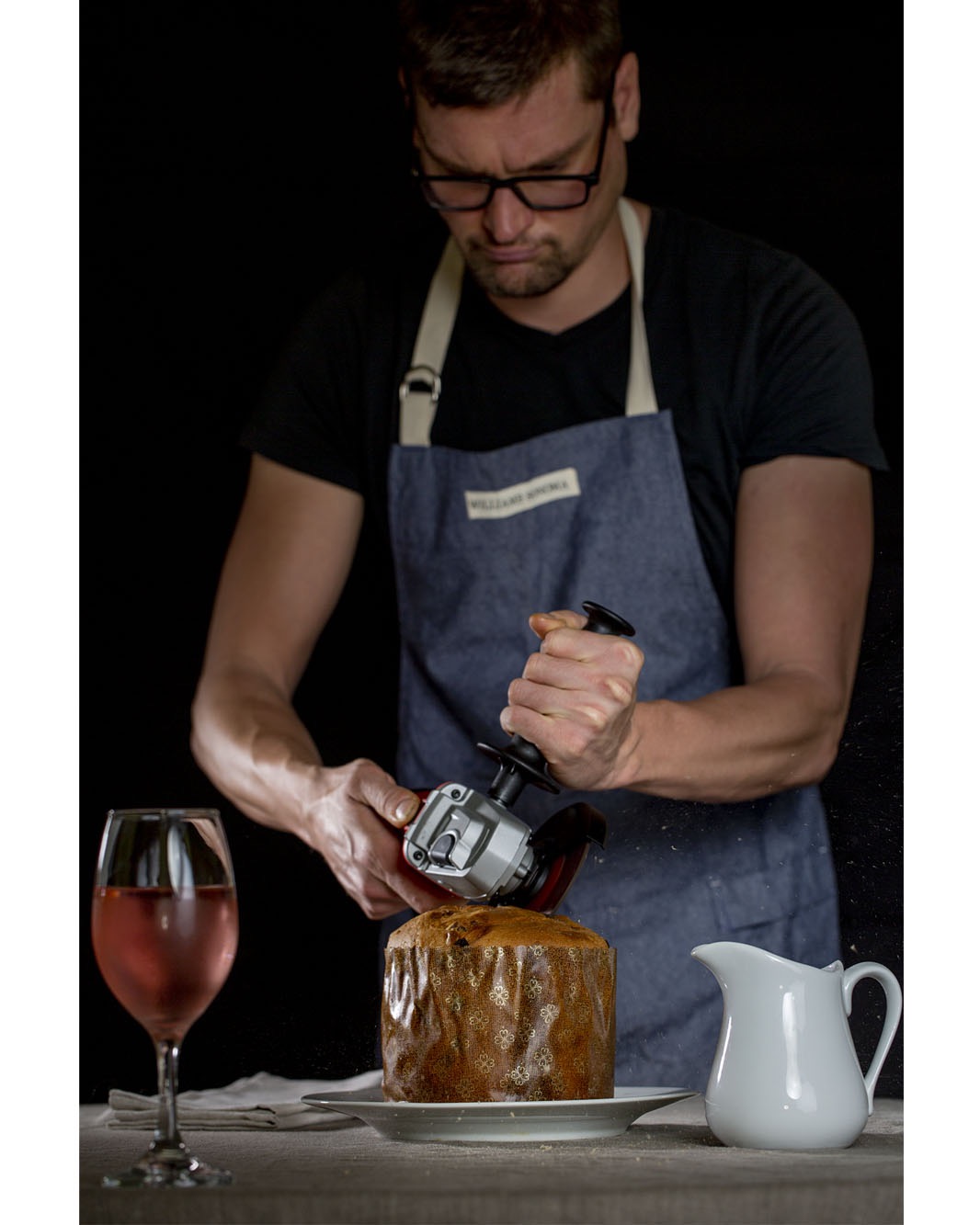 Portrait of the Photographer Will Engelmann wearing an apron and cutting a panettone with a grinder.