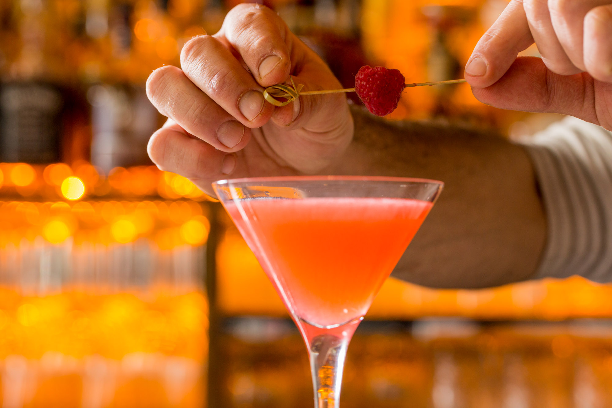 A bartender setting a raspberry garnish on a cocktail.