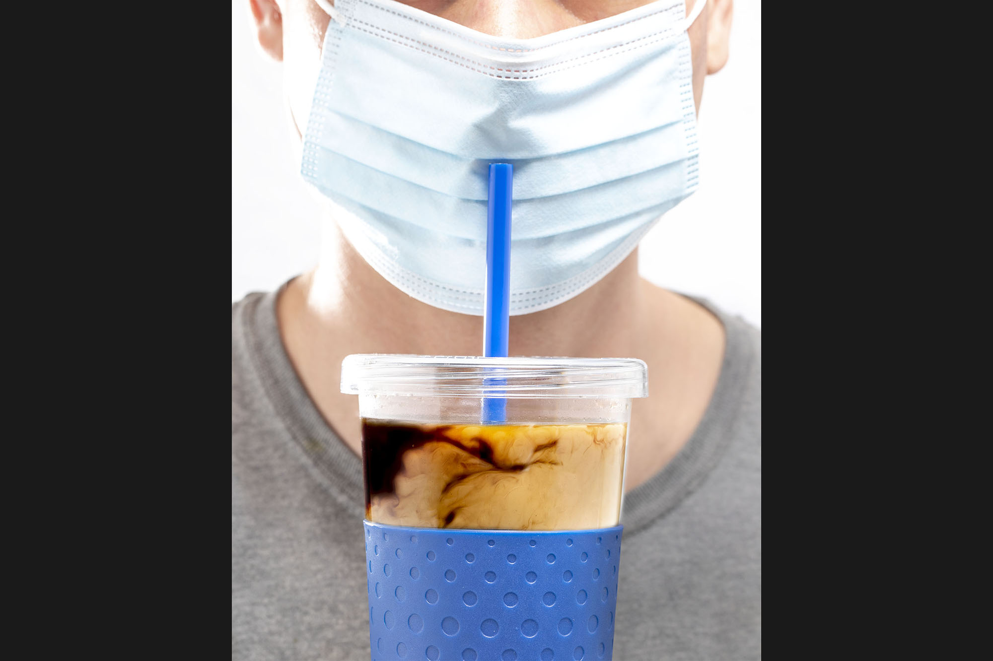 A man trying to drink out of a coffee cup while wearing a face mask
